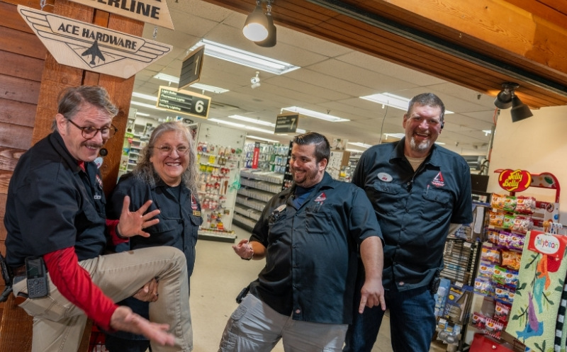 Timberline Ace workers outside shop having fun and pointing to signage